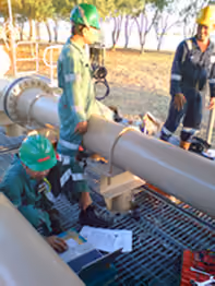 Engineers taking measurements on pipeline metering equipment with a laptop